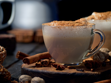 Load image into Gallery viewer, A hot chai latte on a wooden platform, surrounded by cinnamon sticks, nutmeg, and clove.