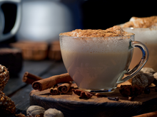 Load image into Gallery viewer, A hot chai latte on a wooden platform, surrounded by cinnamon sticks, nutmeg, and clove.
